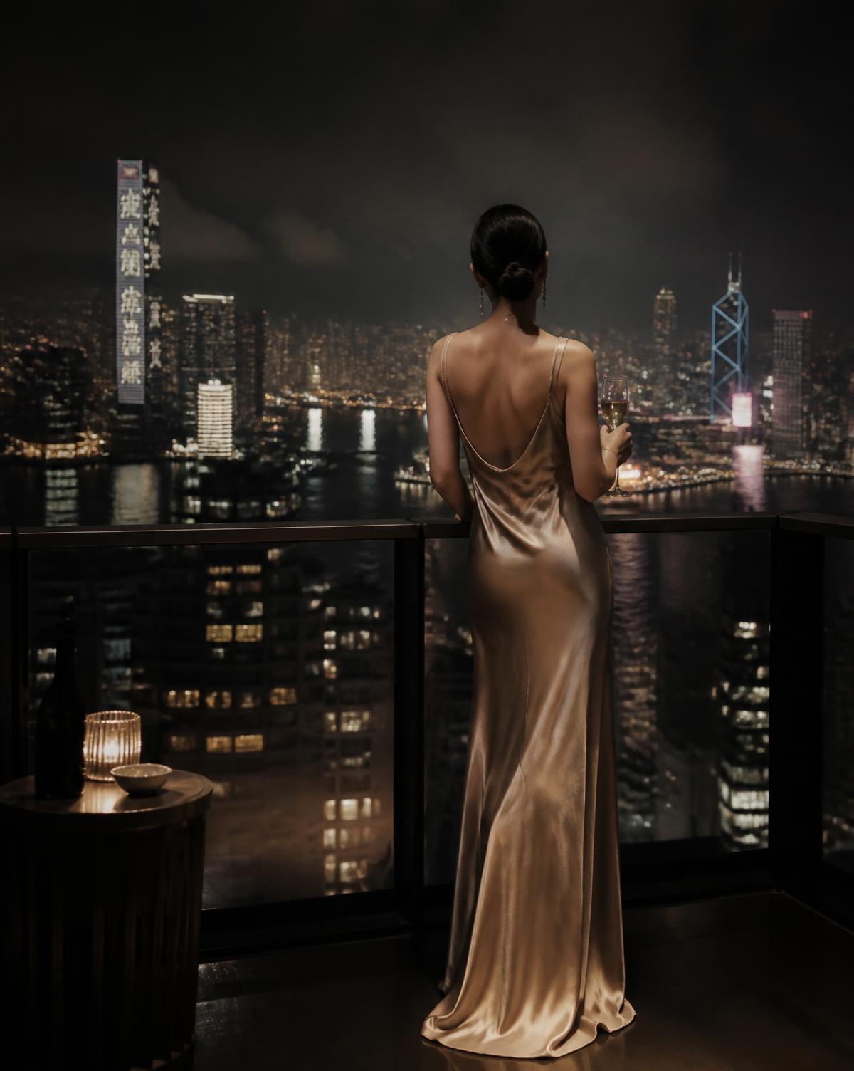 A woman on a hotel terrace above an Asian city at night